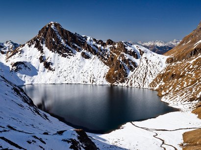I laghi dell‘Alto Adige: meraviglie della natura Lago di montagna circondato da montagne innevate e aree senza neve sotto un cielo sereno