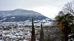 Ihre Hotels in Meran in Südtirol: Hotels im Meraner Land Blick auf eine verschneite Stadt mit Bergen im Hintergrund und Bäumen im Vordergrund