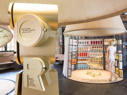 Das Touriseum in Meran Ausstellung mit großem goldfarbenem Buchstabenobjekt und Frau vor Posterwand