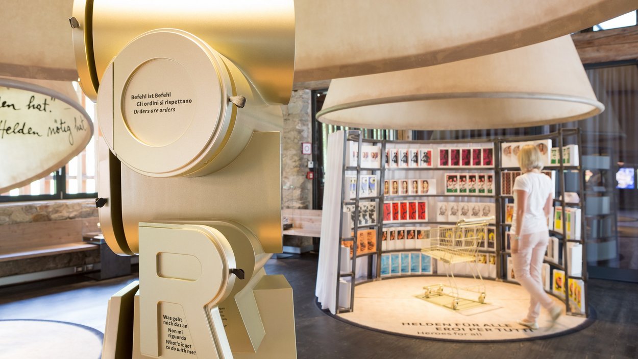 Das MuseumPasseier im Sandhof Ausstellung mit großem goldfarbenem Buchstabenobjekt und Frau vor Posterwand