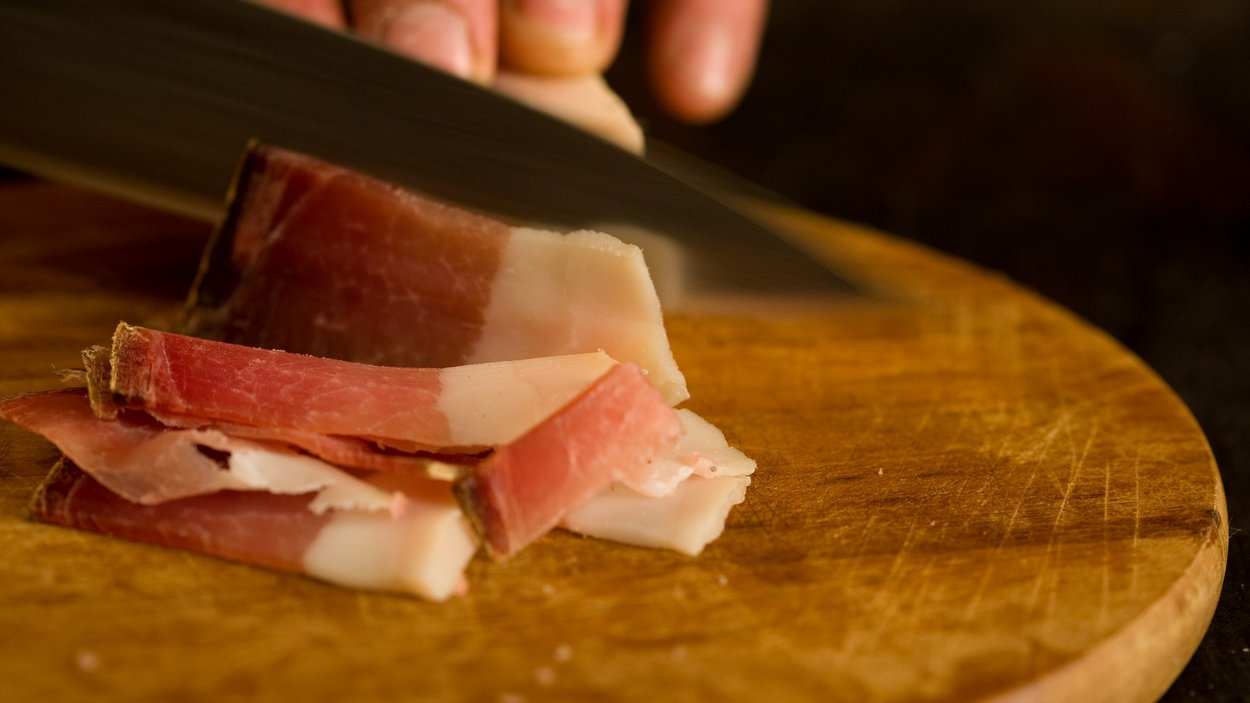 Speckworld a Naturno Mano che taglia fette sottili di pancetta su un tagliere di legno