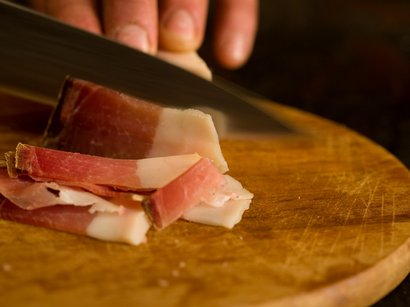 Il MuseoAltaPassiria di Moso in Passiria Mano che taglia fette sottili di pancetta su un tagliere di legno
