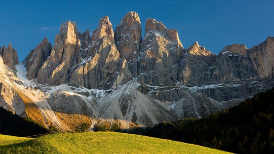 Der Naturpark Puez-Geisler: die „Dolomitenbauhütte“ Sonnige Bergspitzen der Dolomiten über grünem Hang