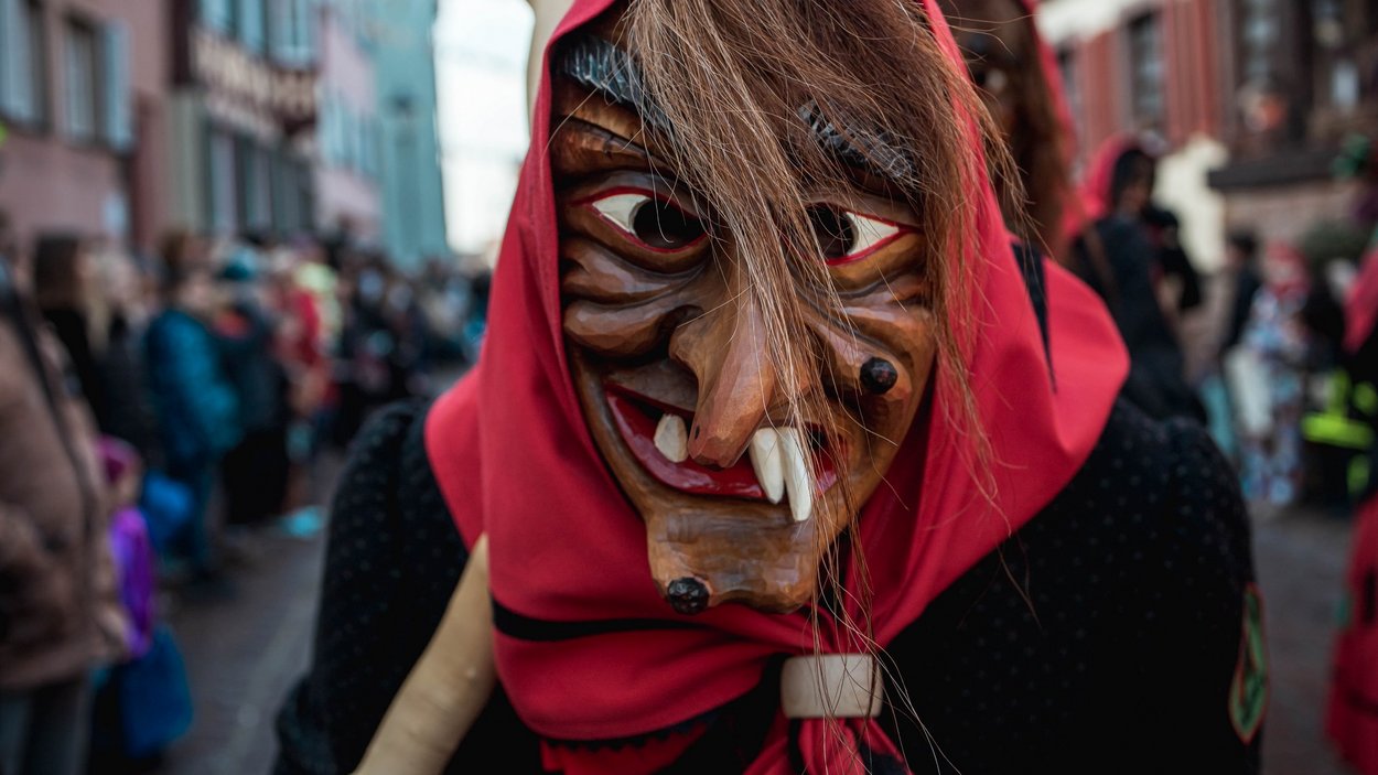 Hexentanz am Würzjoch Hölzerne Hexenmaske mit rotem Kopftuch bei Straßenumzug