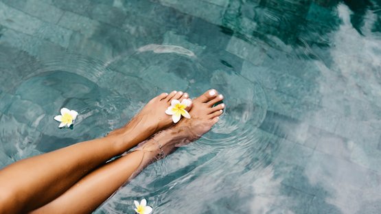Luxushotels in Südtirol - Eleganz & Service Füße im Wasser mit weißen Blumen an einem Pool