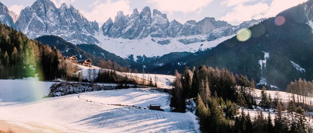 Hotel in Alto Adige 😎☀️ Per vacanze indimenticabili Prato innevato davanti alle Dolomiti con case illuminate dal sole