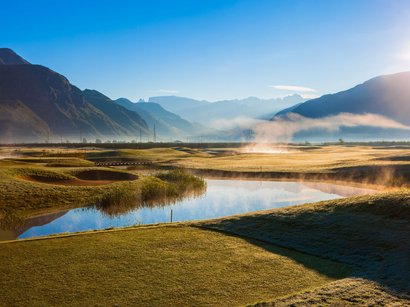 Golfen in Südtirol Golfplatz mit Morgennebel und Bergen im Hintergrund bei Sonnenaufgang