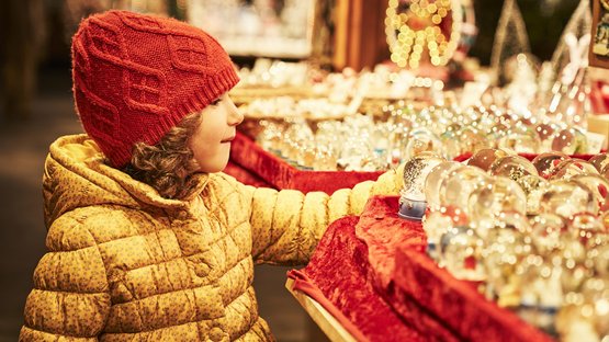Mercatino di Natale di Merano Bambina con cappello rosso guarda sfere di Natale in bancarella