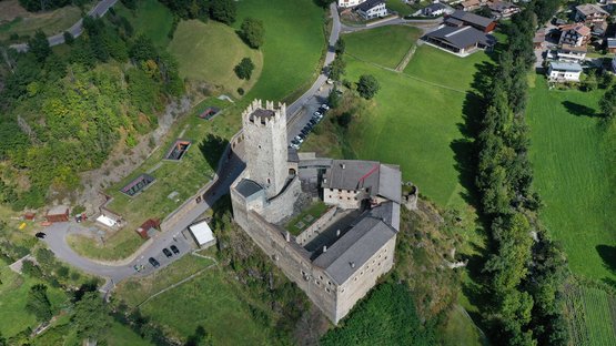 Il Castello del Principe a Burgusio Veduta aerea di un castello su una collina circondato da campi verdi e case