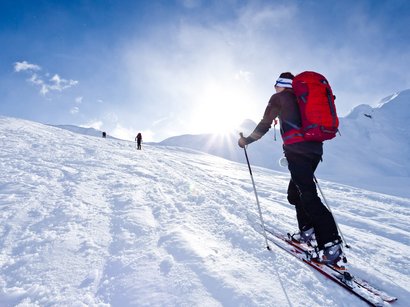 Skihochtour Ortlergruppe: Tag 1 Suldenspitze und Cevedale Skifahrer mit rotem Rucksack auf schneebedecktem Berg bei Sonnenschein