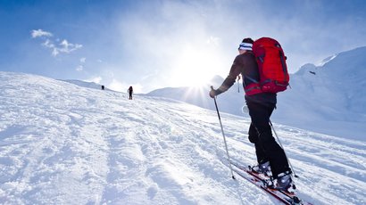 Piz Sesvenna (3204 m.ü.M.) Skifahrer mit rotem Rucksack auf schneebedecktem Berg bei Sonnenschein
