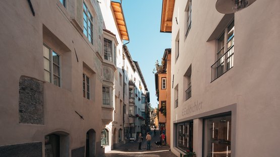 Il Museo Civico di Chiusa Persone in una stretta via soleggiata con edifici storici