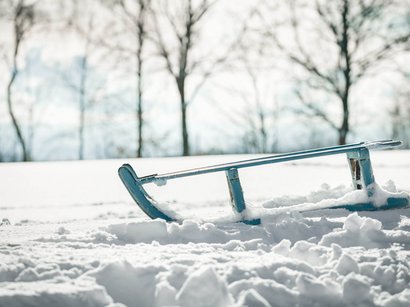 Pista da slittino Malga Geisler Slitta blu nella neve davanti ad alberi spogli sfocati