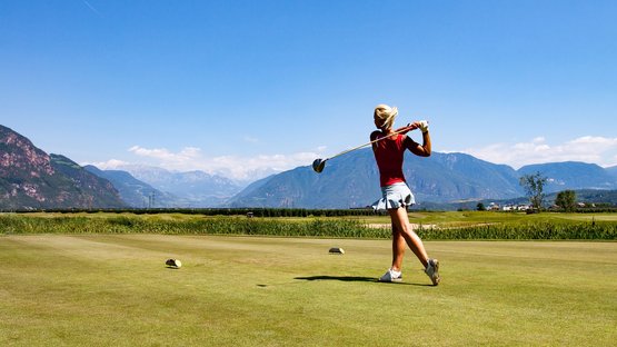 The Blue Monster – il golf club ad Appiano Donna che gioca a golf su un campo con montagne sullo sfondo