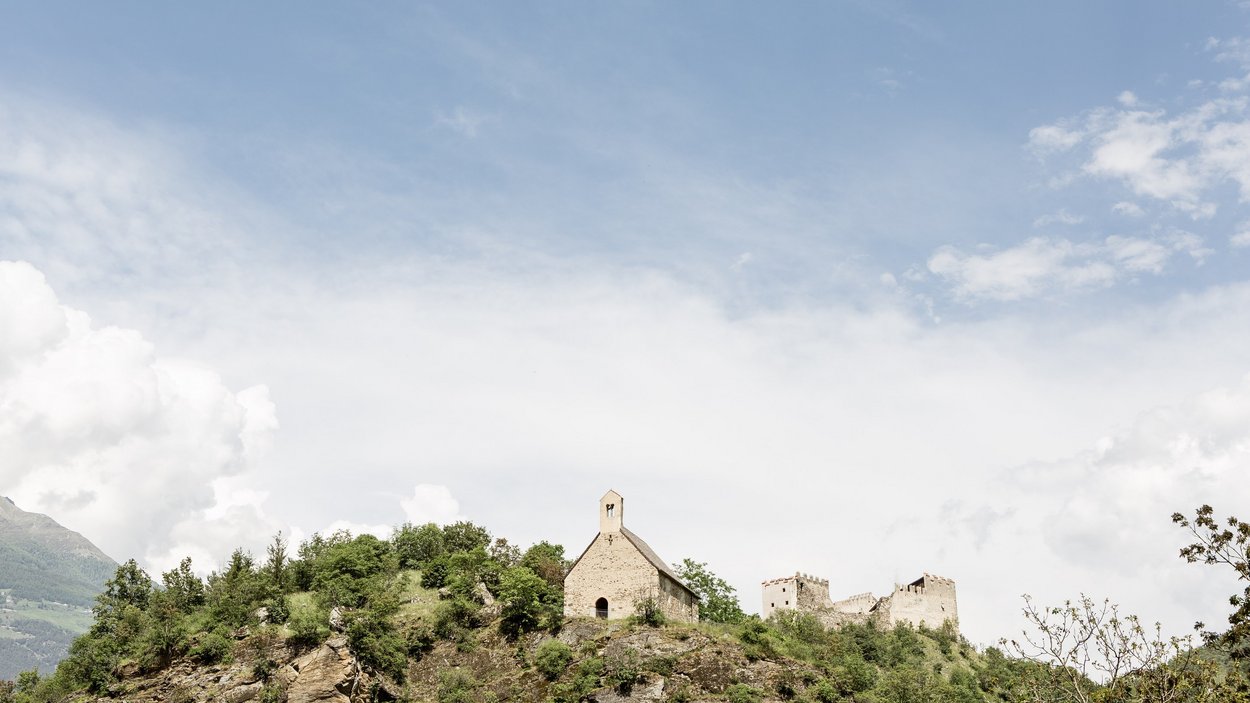 La Cappella di Santo Stefano Vecchia chiesa e rovine di castello su collina boscosa sotto cielo azzurro