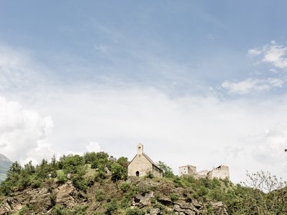 Il centro visitatori Naturatrafoi Vecchia chiesa e rovine di castello su collina boscosa sotto cielo azzurro