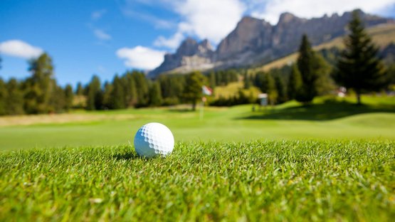 The mountain beast for golfers Golfball auf Gras mit Bergen und blauem Himmel im Hintergrund