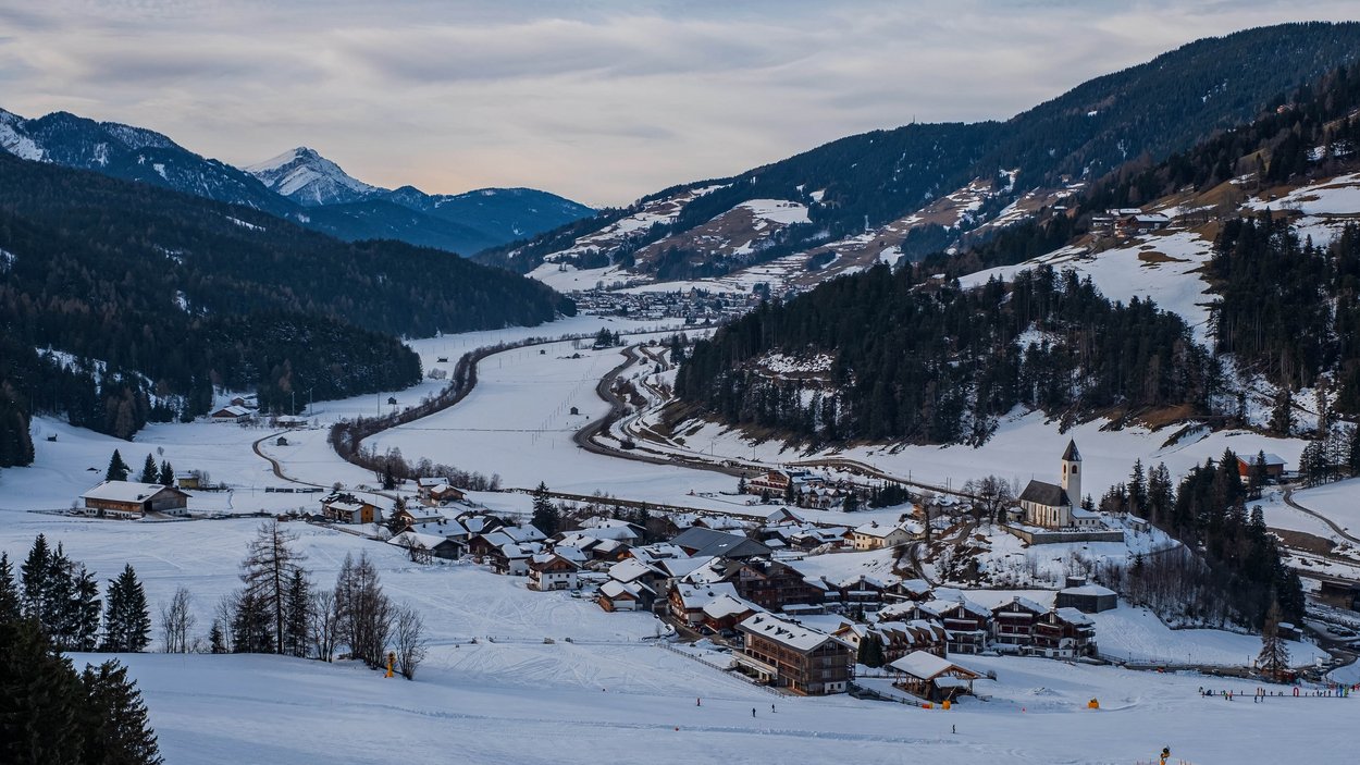 Rodelspaß bei Innichen Verschneites Bergdorf in einem Tal mit Bergen im Hintergrund