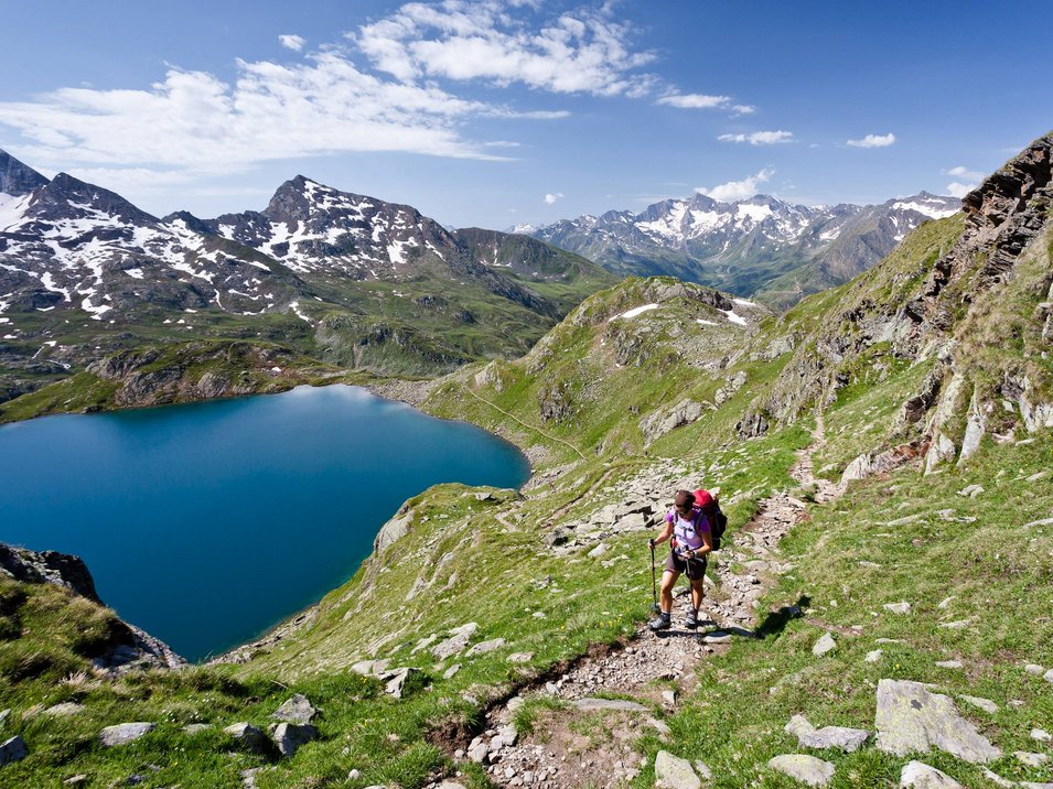Hotel per escursionisti in Alto Adige Escursionista su sentiero montano con vista su lago e cime innevate