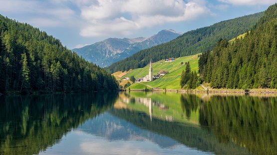 Rund um den Durnholzer See Bergsee mit Wald und Dorf mit Kirche im Tal unter blauem Himmel