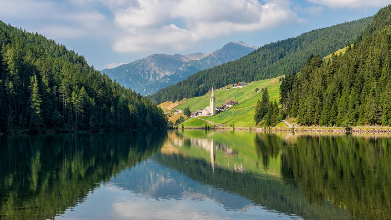 Sulle sponde del Lago di Valdurna Lago alpino con foresta e villaggio con chiesa nella valle sotto il cielo azzurro