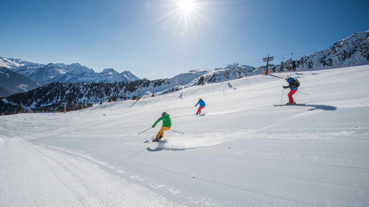 Das beliebte Skigebiet im Tauferer Ahrntal Drei Skifahrer fahren bei sonnigem Wetter auf einer schneebedeckten Piste in den Bergen