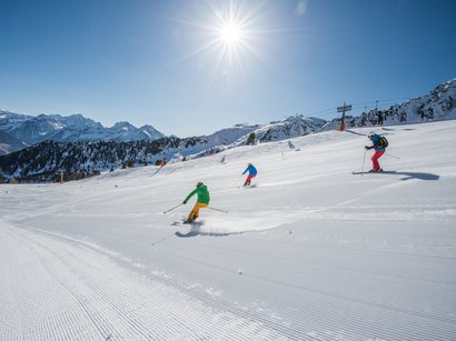Das Skigebiet Kronplatz im Herzen der Dolomiten Drei Skifahrer fahren bei sonnigem Wetter auf einer schneebedeckten Piste in den Bergen