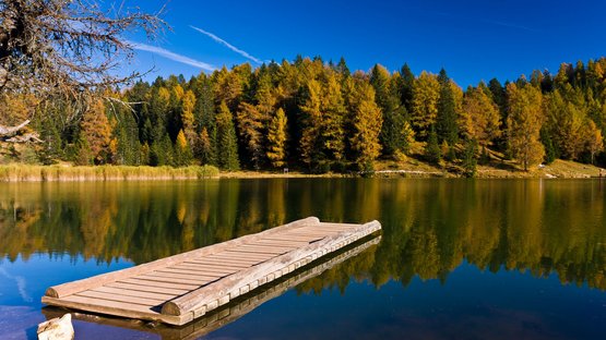Lago di Santa Maria: che pace! Pontile di legno su lago calmo con foresta autunnale e cielo blu sullo sfondo