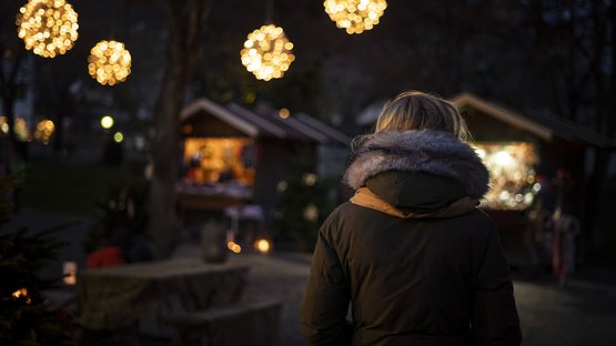 Der Weihnachtsmarkt in Klausen Person in Winterjacke bei beleuchtetem Weihnachtsmarkt am Abend