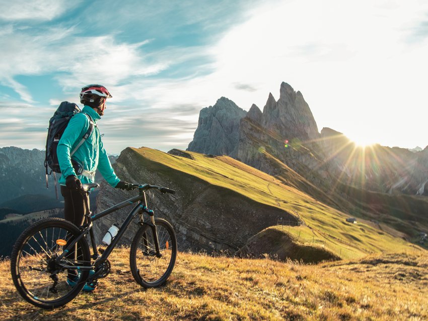Hotel in Alto Adige 😎☀️ Per vacanze indimenticabili Ciclista con casco osserva un panorama montano al tramonto