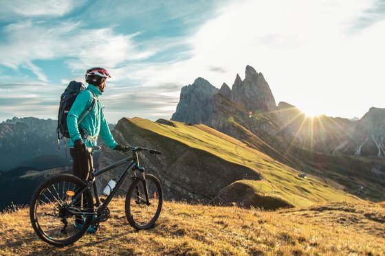 Bikehotel in den Dolomiten, im Meraner Land und, und, und Radfahrer mit Helm schaut auf Bergpanorama bei Sonnenuntergang