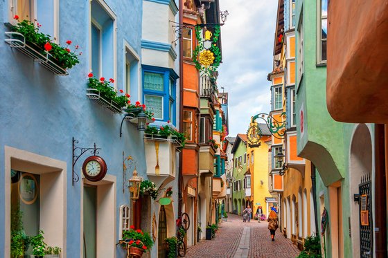 Trentino-Südtirol entdecken Bunte Altstadtgasse mit Blumen und Passanten auf Kopfsteinpflaster