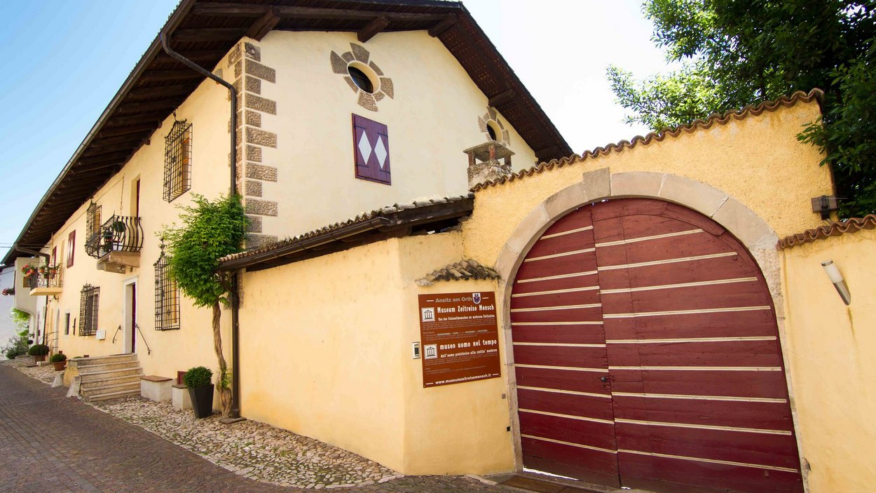Il museo Uomo nel tempo a Cortaccia Edificio storico con grande porta rossa e cartelli su strada lastricata