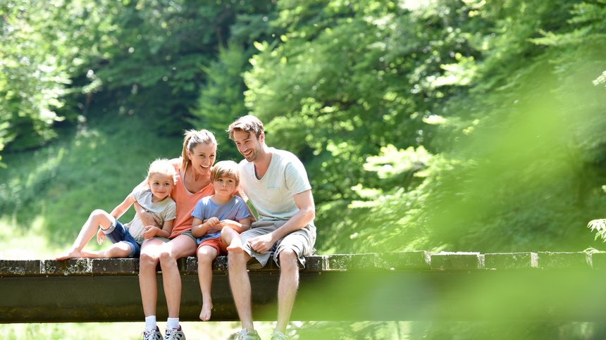 Hotel in Alto Adige 😎☀️ Per vacanze indimenticabili Famiglia felice con due bambini seduta su un ponte in mezzo alla natura