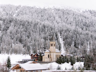 Stilfser Joch – Königin der Passstraßen Kirche im verschneiten Dorf vor bewaldetem, schneebedecktem Berg