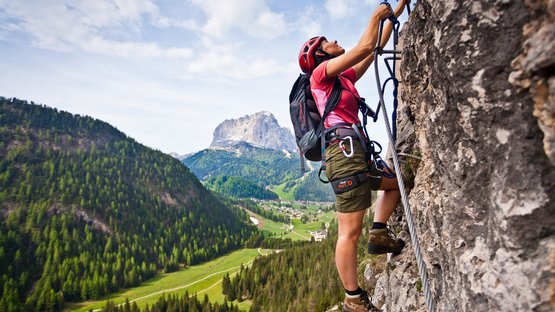 Klettern Südtirol – es geht hoch hinaus! Frau klettert mit Helm und Ausrüstung an Felswand in den Bergen