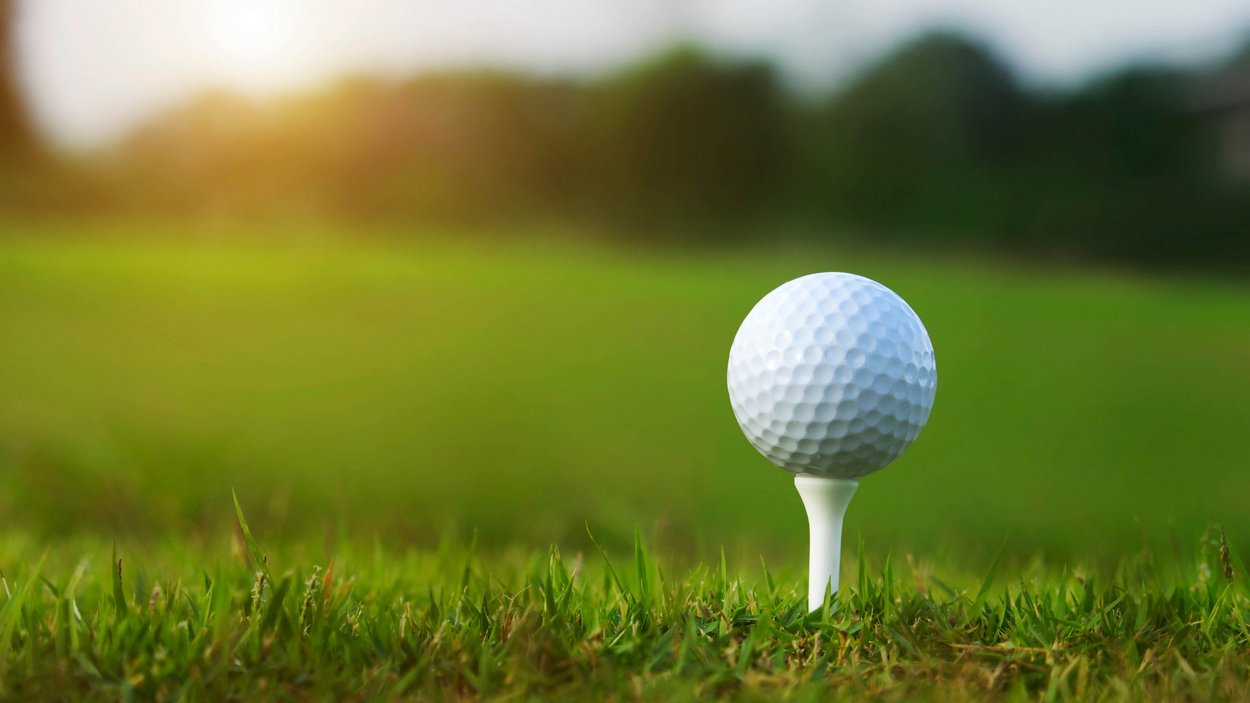 Golfen in Südtirol Golfball auf Tee im grünen Gras eines Golfplatzes bei Sonnenlicht