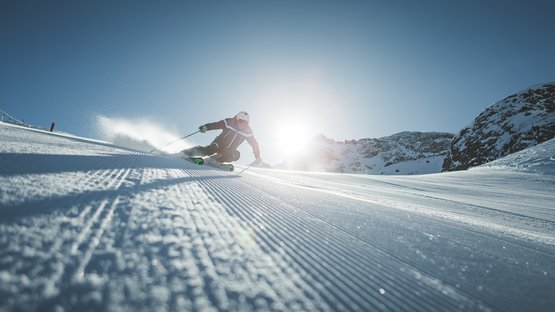 Ski-in/Ski-out in Südtirol Skifahrer bei Abfahrt auf präparierter Piste mit Sonne und Bergen im Hintergrund