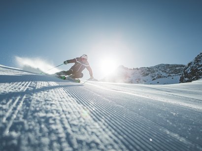 Aktivurlaub in Südtirol Skifahrer bei Abfahrt auf präparierter Piste mit Sonne und Bergen im Hintergrund
