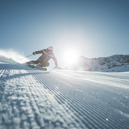 Drei Zinnen-Schneeschuhwanderung Skifahrer bei Abfahrt auf präparierter Piste mit Sonne und Bergen im Hintergrund
