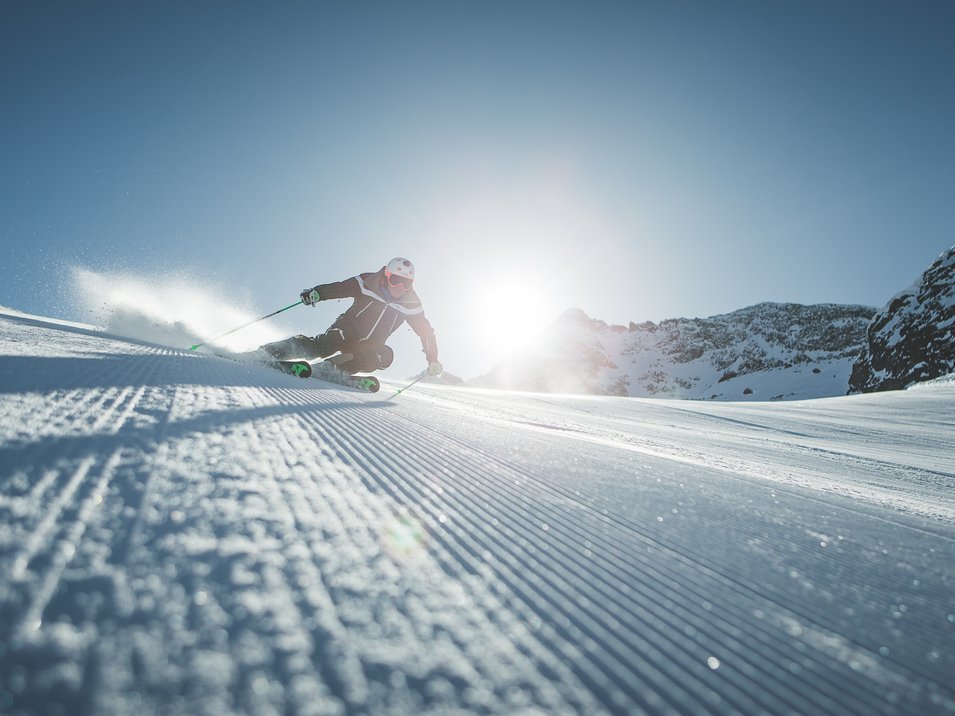 Ski-in/Ski-out in Südtirol Skifahrer bei Abfahrt auf präparierter Piste mit Sonne und Bergen im Hintergrund