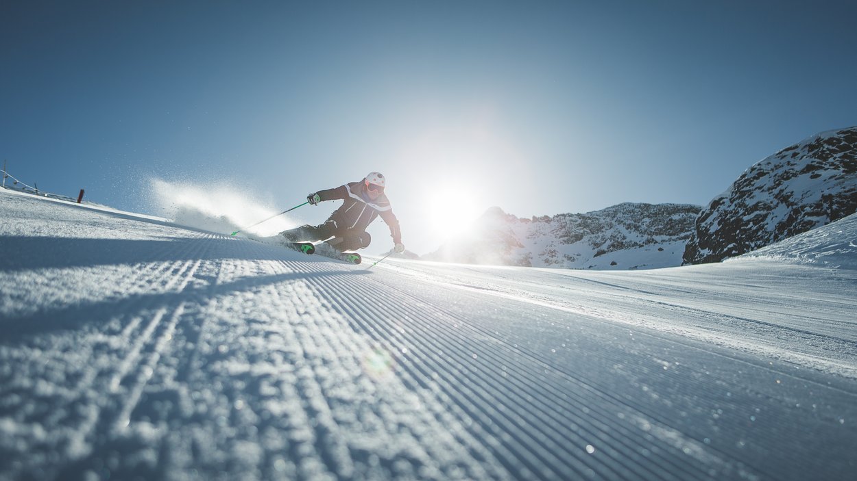Skiurlaub in Südtirol: Pistengaudi und Schneespaß Skifahrer bei Abfahrt auf präparierter Piste mit Sonne und Bergen im Hintergrund