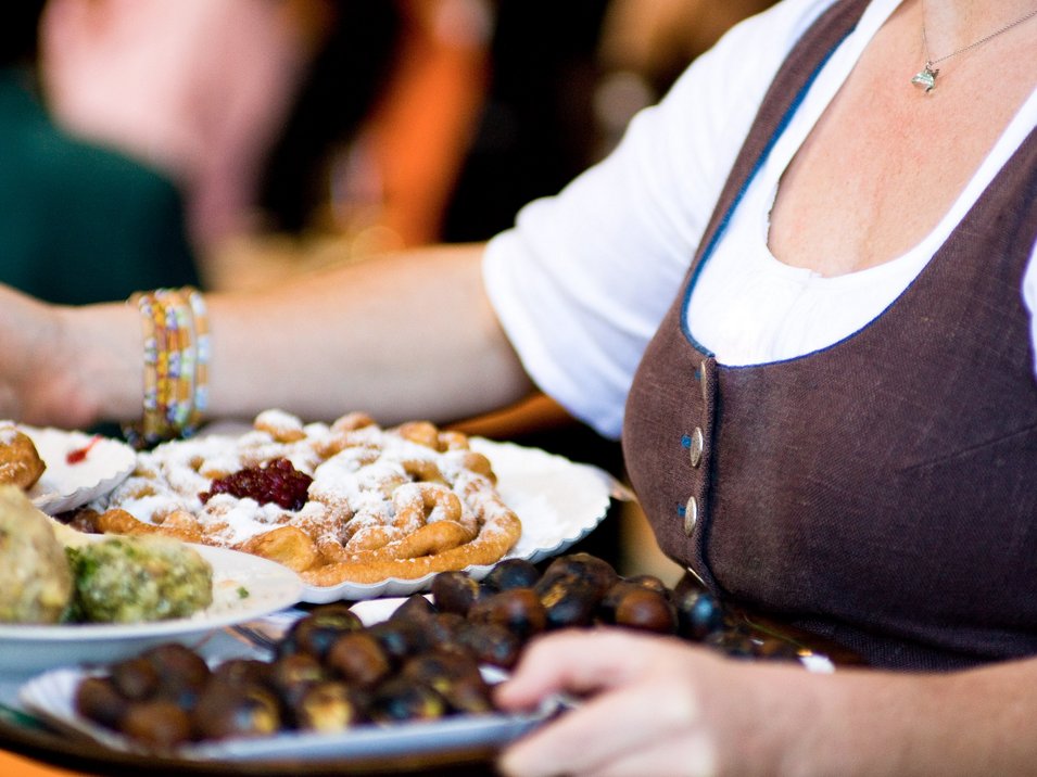 Mercati contadini in Alto Adige Donna che porta piatti con varie pietanze tradizionali spolverate di zucchero a velo