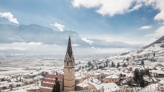 Hotel a Bolzano e dintorni Villaggio innevato con campanile davanti a montagne e cielo azzurro