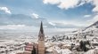Hotel a Bolzano e dintorni Villaggio innevato con campanile davanti a montagne e cielo azzurro