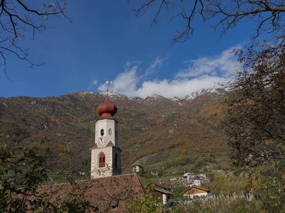 Vie ferrate in Alto Adige Campanile con cupola rossa di fronte a montagne autunnali e cielo blu limpido