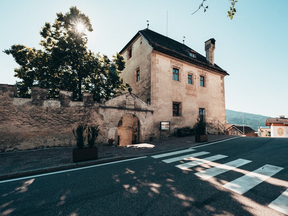 Die Hotels in Feldthurns stehen für einen traumhaften Urlaub Altes Gebäude mit Mauereingang an sonnigem Tag und Zebrastreifen vor der Straße