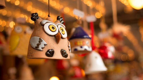 Das Rittner Christbahnl Ton-Eulenfigur hängt an einem Draht vor unscharfem Hintergrund mit Lichtern