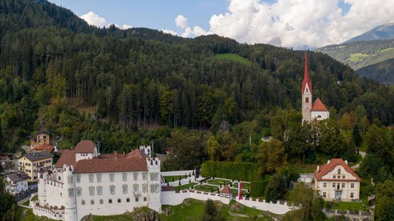 Schloss Ehrenburg im Pustertal Schloss und Kirche auf bewaldetem Hügel unter blauem Himmel mit Wolken