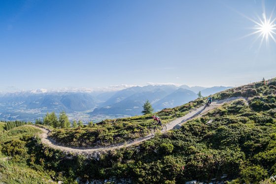 Bikehotel in den Dolomiten, im Meraner Land und, und, und Zwei Mountainbiker auf einem Bergpfad bei Sonnenschein mit Alpenpanorama